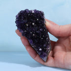 Hand holding dark purple amethyst crystal rock against a light blue background