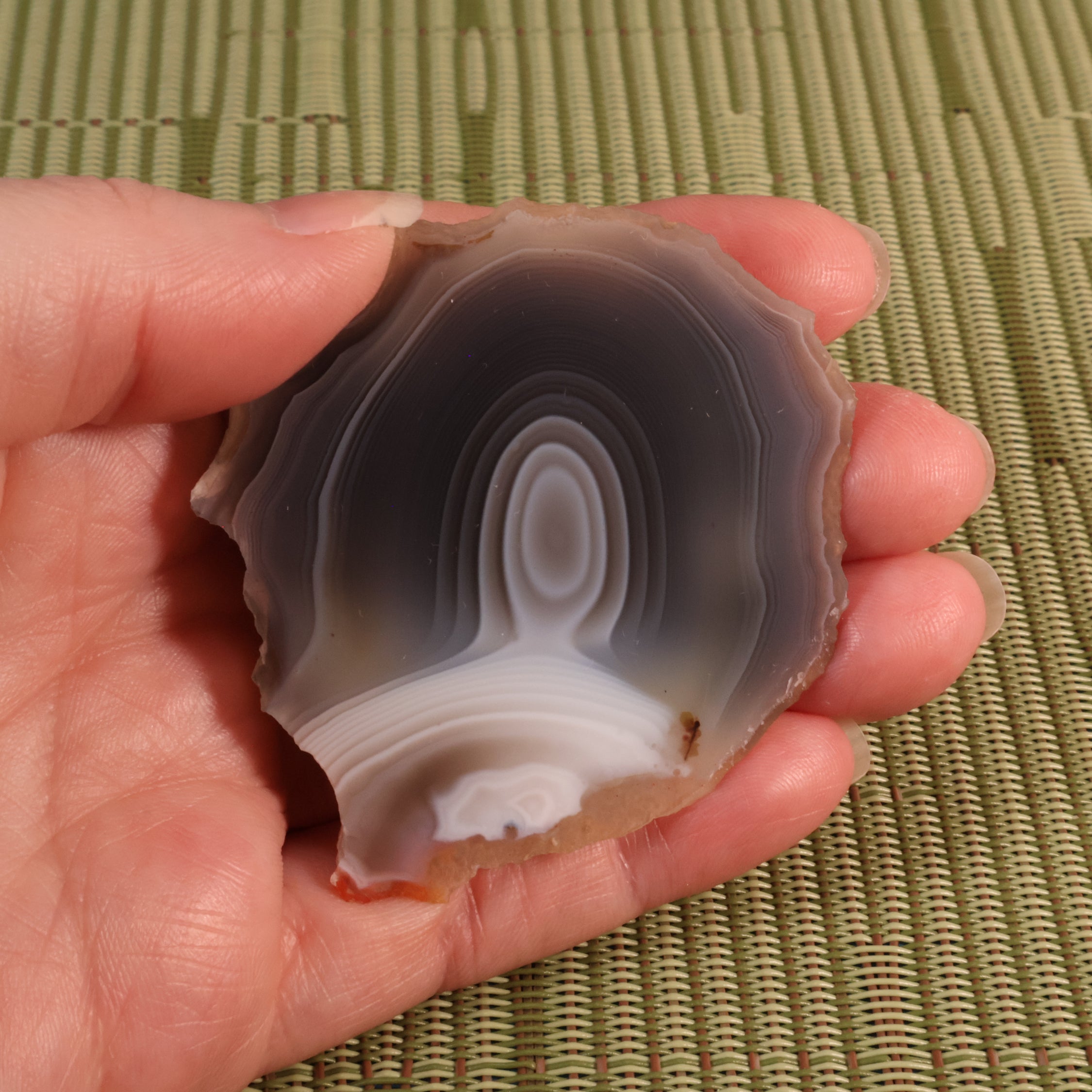 Hand holding a polished botswana agate stone with concentric patterns against a green woven mat background