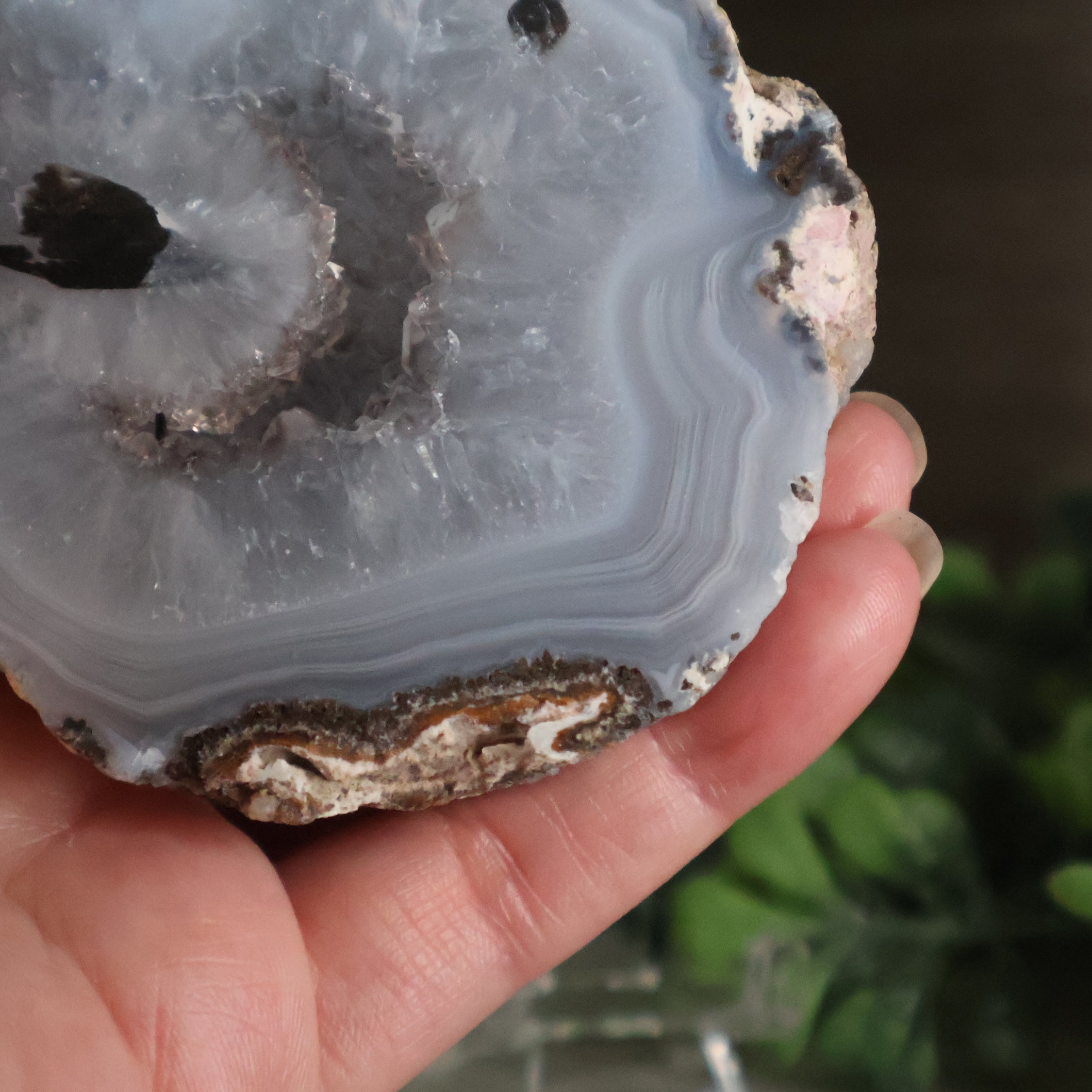 Close-up of a hand holding a geode crystal with concentric layers and a dark center.