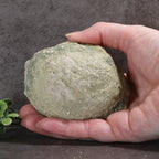 Hand holding a large greenish-brown rock against a dark background