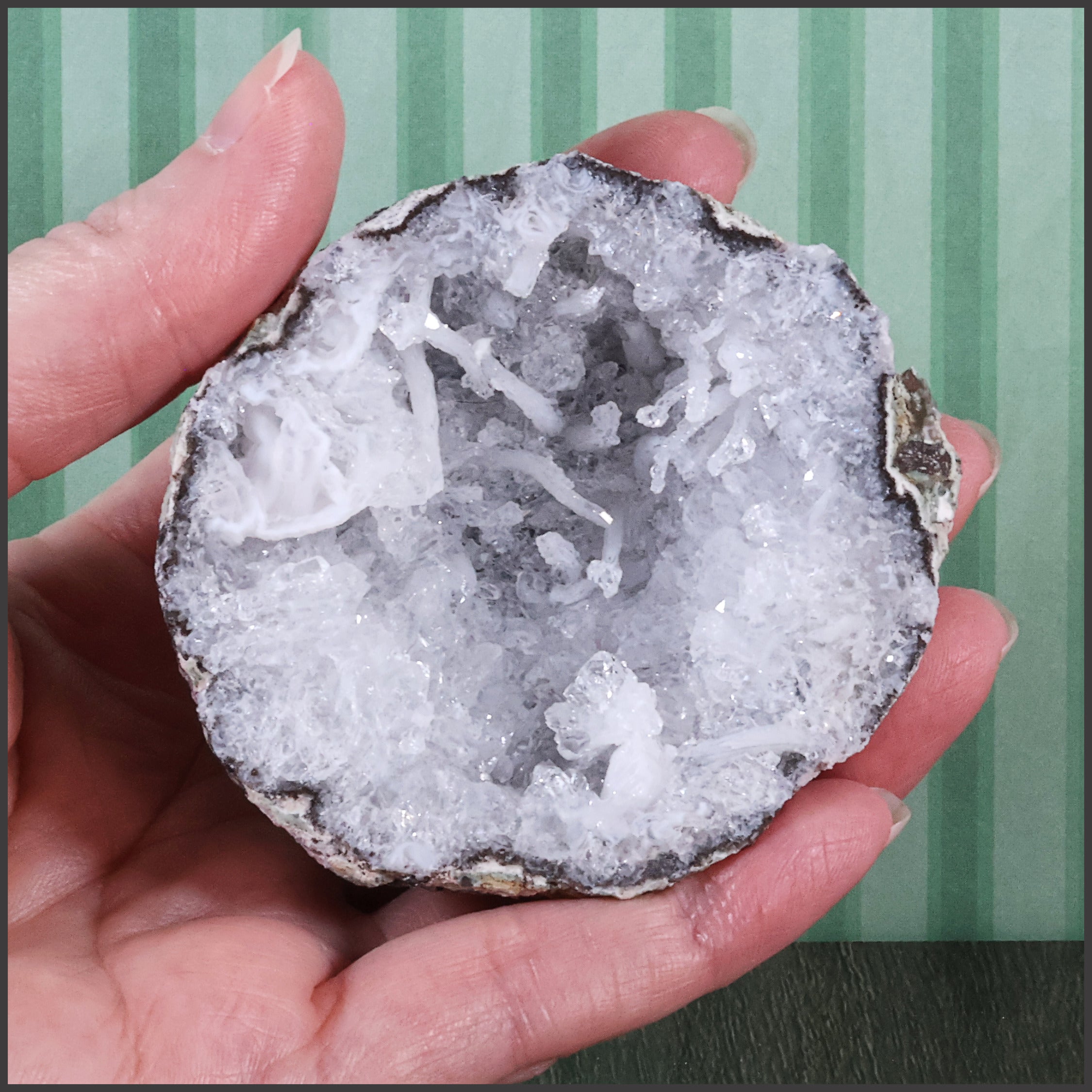 Hand holding a crystal geode against a striped background
